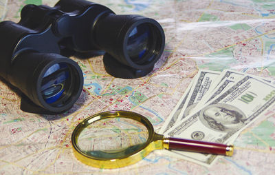 Magnifying glass with paper currency and binoculars on map