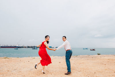 Rear view of couple holding hands while standing on beach against sky