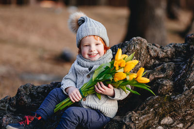 Portrait of boy holding flowers bouquet while sitting by rock