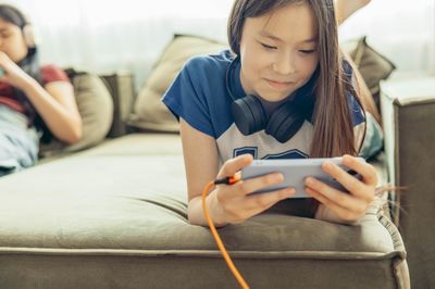 Portrait of young woman using mobile phone while lying on sofa at home