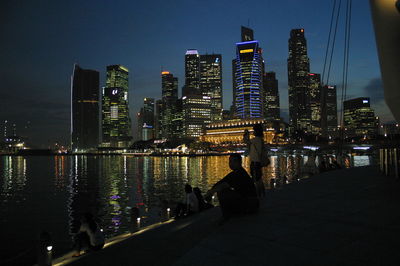 People on footpath by singapore river in city at night