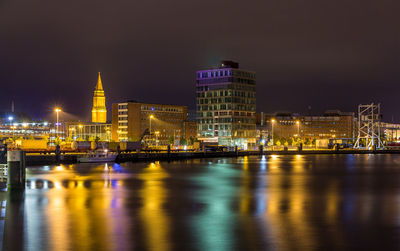 Illuminated city by sea against sky at night