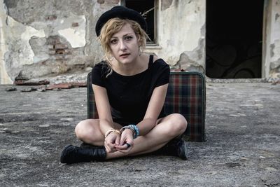 Portrait of young woman sitting on sidewalk in city