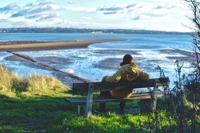 Rear view of man sitting on sea shore against sky