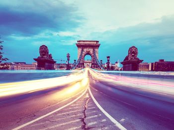 Light trails on road against cloudy sky