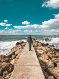 Rear view of woman standing on rock at beach against sky