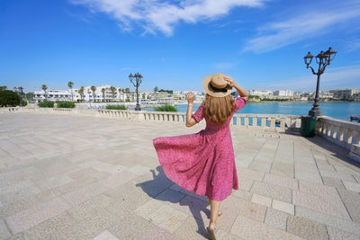 Rear view of woman standing at beach against sky
