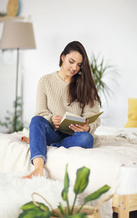 Young woman sitting on book at home