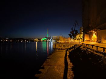 Illuminated pier by river against sky at night