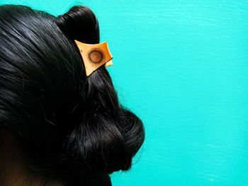 Cropped image of woman with black hair against turquoise background