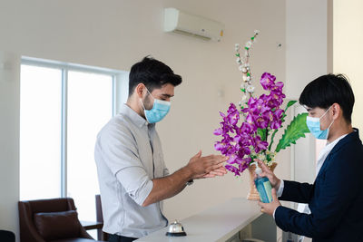Side view of young businessman wearing mask using hand sanitizer at hotel reception