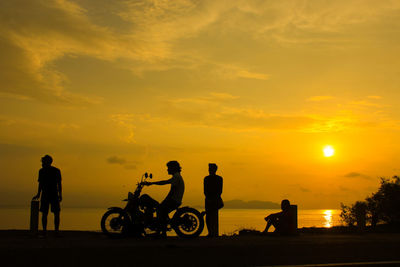 Silhouette people riding bicycle against sky during sunset