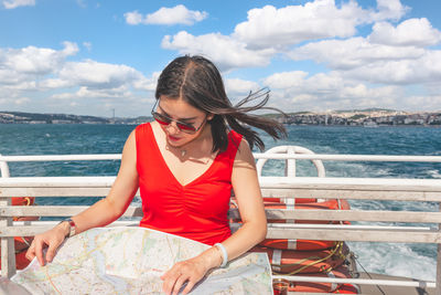 Woman looking at map while sitting by railing in nautical vessel on sea