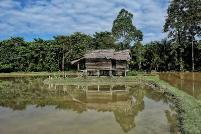 Gazebo by lake against building and trees against sky