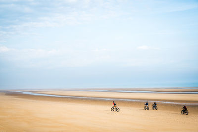 People cycling at beach against sky