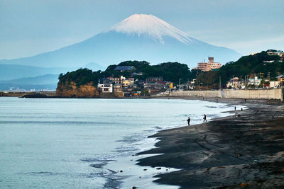 Scenic view of sea and snow covered mountain by city against sky in the morning