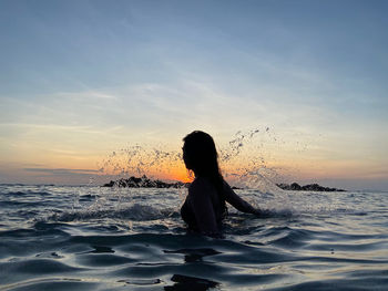 Silhouette woman in sea against sky during sunset