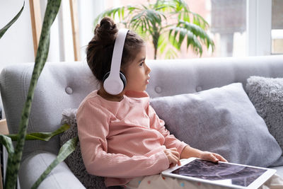 Girl wearing headphones looking away while sitting on bed