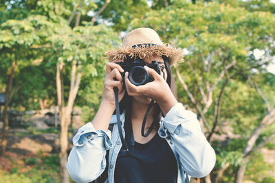 Young woman photographing through camera against trees