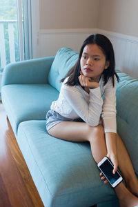 Asian teenage girl sitting on sofa watch television