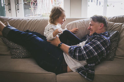 Father playing with girl on sofa at home