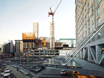 Modern buildings in city against sky with cranes