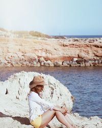 Woman sitting on beach by sea against sky