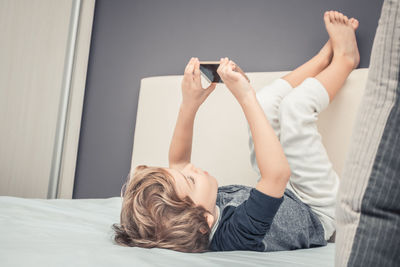 Boy playing on mobile while lying on bed with feet up at home