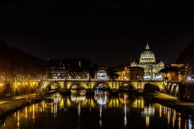 Illuminated bridge over river by buildings against sky at night