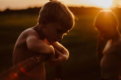 Side view of shirtless boy on field during sunset