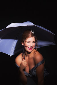 Portrait of smiling young woman under umbrella over black background