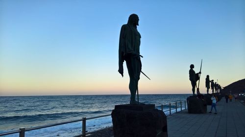 Rear view of silhouette man walking at beach against clear sky