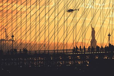 Silhouette of brookllyn bridge against statue of liberty during sunset