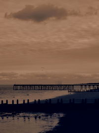 Silhouette bridge over sea against sky during sunset