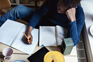 High angle view of teenage boy writing on book while doing homework