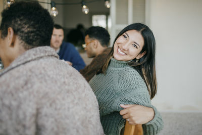 Smiling woman leaning back while sitting with male friends in patio