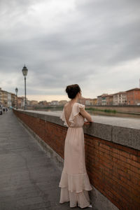 Woman standing at railing in city against cloudy sky