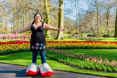 Full length of a latin woman in black dress, jeans and giant wooden shoes, red and yellow flowers