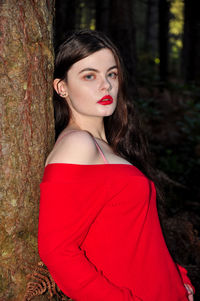 Portrait of young woman leaning on tree at forest