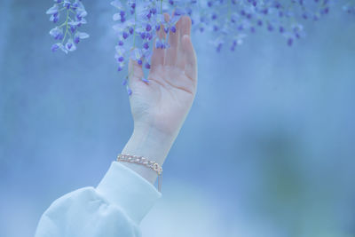 Close-up of woman holding hands against blue sky