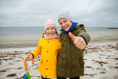Portrait of smiling boy with sister showing thumbs up sign at beach