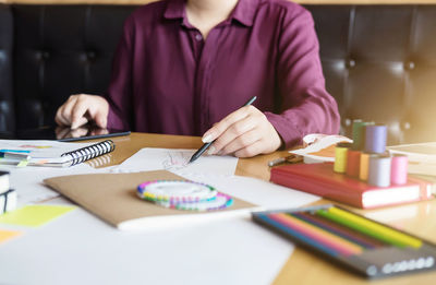 Midsection of fashion designer sketching on paper in office