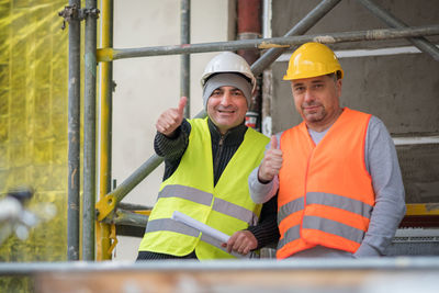 Portrait of engineers gesturing thumbs up sign while standing at construction site