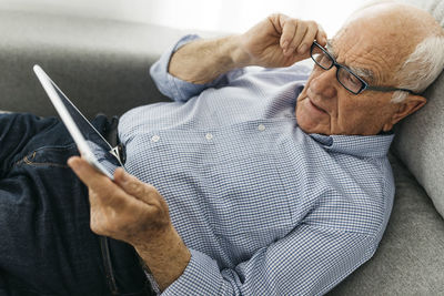 Senior man surfing the internet on a tablet while lying on the sofa