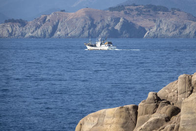 Boat sailing on sea by mountains against sky