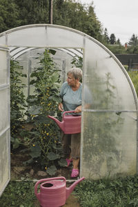 Senior woman with watering can in greenhouse