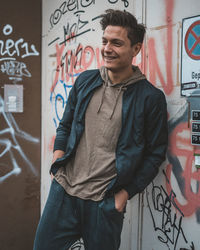 Portrait of young man standing against graffiti wall