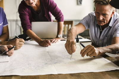 Female instructor guiding senior men using drawing compass on map at table during navigation course