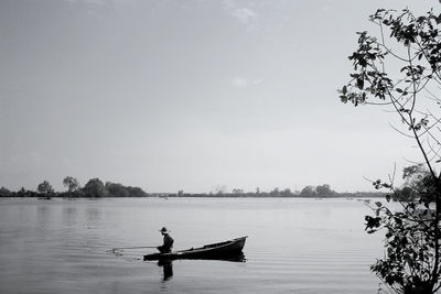 Man sitting on boat in lake against sky