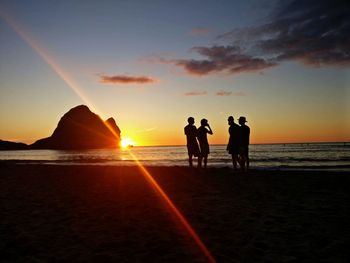 Silhouette people on beach against sky during sunset